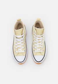 Höga sneakers i gul canvas med vita snören och gummisulor. Har en svart linje och orange gummidetaljer.