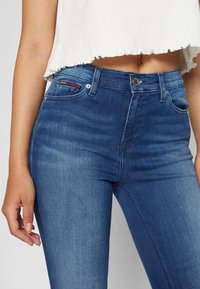 Jeans de mezclilla azul oscuro con una cintura alta, que presentan un sutil desgastado, cinco bolsillos y un cierre de botón plateado.