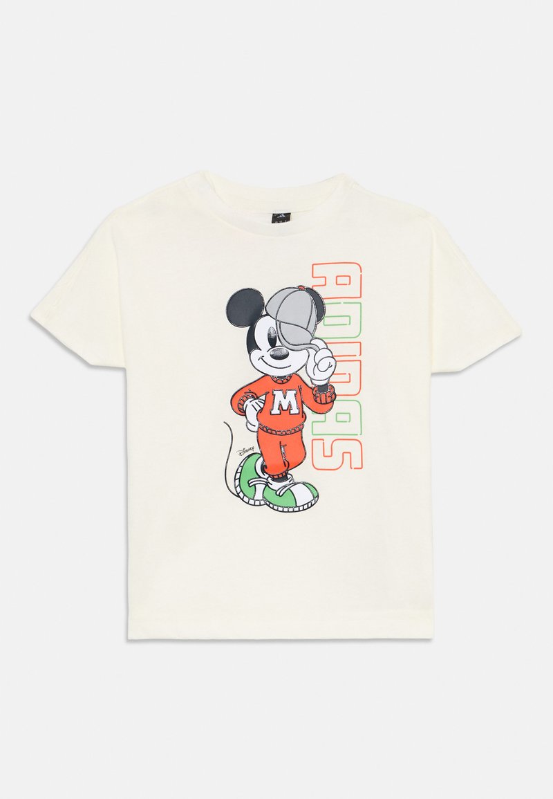 Camiseta crema con un ratón de dibujos animados vestido con un chándal naranja, zapatillas verdes y una gorra, acompañado de un colorido texto "ADIDAS".
