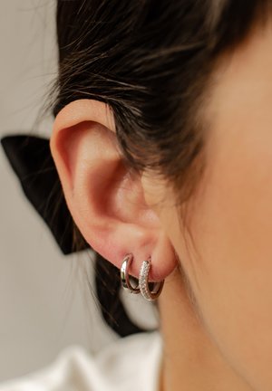 Silver hoop earrings with a textured finish and clear accents, displayed on an ear. Includes a small, polished hoop layered beneath.
