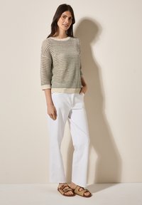 Pull en maille légère beige à tricot ouvert, manches trois-quarts, associé à un pantalon droit blanc et des sandales à glisser marron.