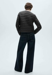 Jachetă puf cu un design negru, cu textură matlasată orizontală, asortată cu blugi întunecați cu croială largă. Design minimalist, fără branding sau accente vizibile.