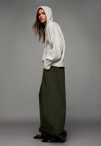 Felpa oversize grigio chiaro con finitura texturizzata, abbinata a pantaloni a gamba larga verde oliva a vita alta e ballerine nere con punta.