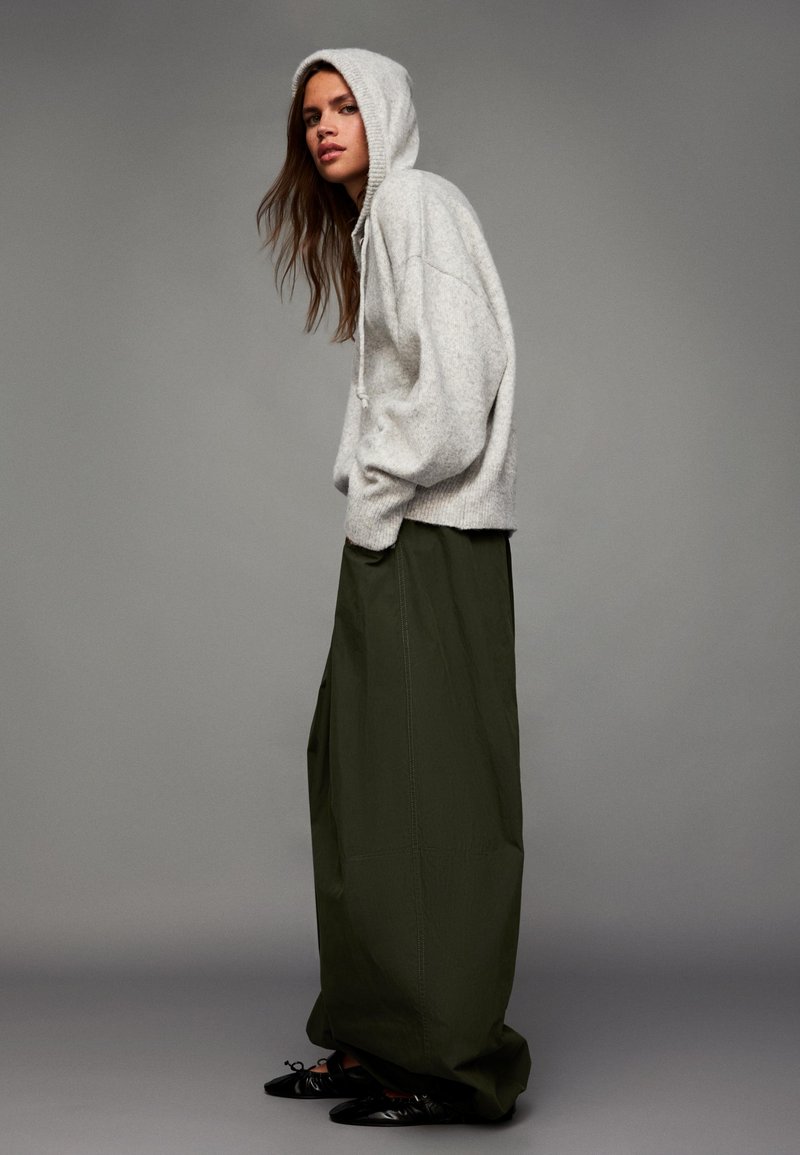 Felpa oversize grigio chiaro con finitura texturizzata, abbinata a pantaloni a gamba larga verde oliva a vita alta e ballerine nere con punta.