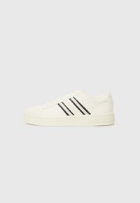 White canvas sneakers with a round toe, three black stripes, and a textured rubber sole. Branding on the side and heel.