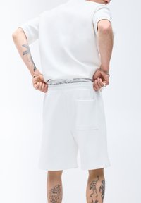 Polo à manches courtes blanche et shorts assortis en tissu doux, avec une taille élastique et une poche arrière sur les shorts.