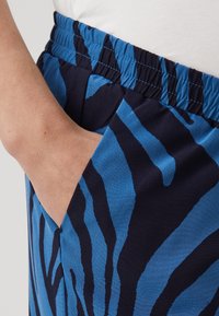 Blue and navy patterned joggers with an elastic waistband, featuring a side pocket and smooth texture, highlighted by vertical stripes.