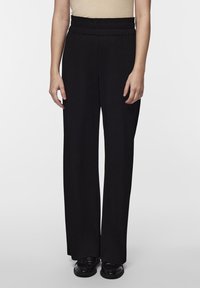 Pantalons larges noirs avec une texture côtelée, dotés d'une taille haute élastique et d'une coupe droite. Portés avec des chaussures plates noires.