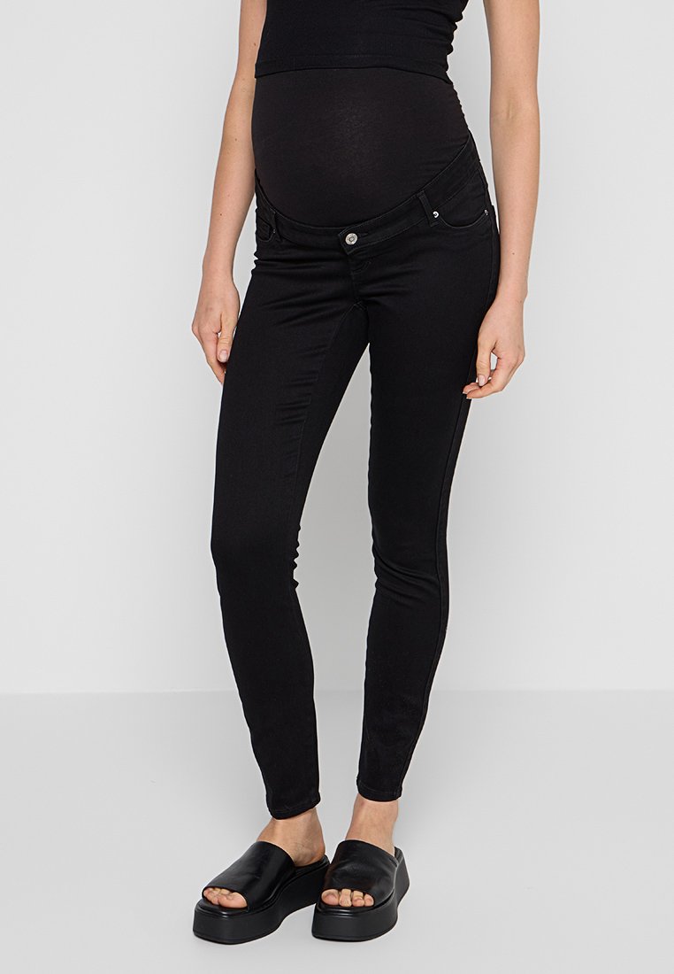 Zwarte zwangerschapsjeans met een aansluitend ontwerp, voorzien van een stretchy tailleband en zijzakken, gecombineerd met platte zwarte instapsandalen.