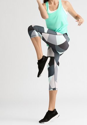 Débardeur sportif en maille turquoise, associé à des leggings 3/4 noirs à motif géométrique. Des chaussures de sport noires complètent l'ensemble.