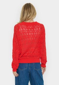 Piros kötött pulóver csipke mintával, bordás mandzsettákkal és hemline-nal, laza szabással. A háta részben áttetsző, nyitott dizájnú.
