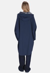 Tengerészkék esőkabát kapucnival, laza szabással. Csillogó bélés és hosszú ujj jellemzi, sötét farmerrel párosítva.