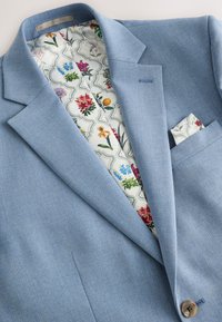 Blazer azzurro chiaro con esterno strutturato. L'interno presenta una fodera a motivo floreale e un fazzoletto da taschino con design coordinato.