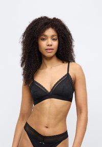 Mustast pitsist rinnahoidja, millel on kolmnurkse kujuga tassid, reguleeritavad rihmad ja notitud ääris; sobitatud samas stiilis pitsdetailidega püksikutega.