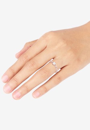 Anello d'argento su una mano con tre piccole pietre. La fascia ha un design elegante e minimalista, con una texture liscia e una finitura lucida.
