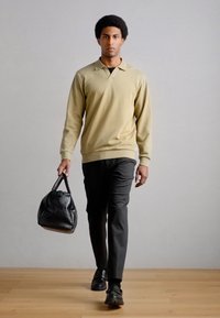 Bézs poló pulóver, fekete nadrág és fekete mintás táska. A modell fekete cipőt visel, sima textúrával és egyszerű dizájnnal.