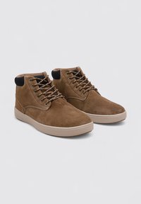 Botas de tobillo de ante marrón con acentos de tela negra, diseño de cordones y suelas de goma beige. Presenta una textura suave y costuras sutiles.