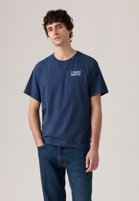 Μπλε ναυτικό βαμβακερό t-shirt με κοντά μανίκια, στρογγυλή λαιμόκοψη και μικρό λευκό λογότυπο Levi's στο στήθος. Φορεμένο με μπλε τζιν από denim.