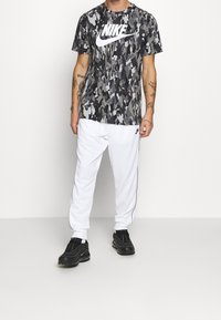 Svart och grå kamouflage Nike t-shirt med vit logotyp, tillsammans med vita träningsbyxor och svarta sportskor. Texturerat material, avslappnad passform.