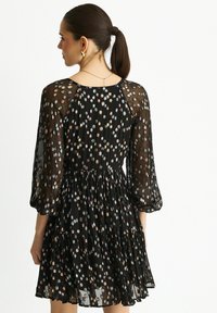 Black sheer dress with three-quarter sleeves, featuring colorful floral patterns and a tiered skirt design. Accentuated with a subtle sheen.