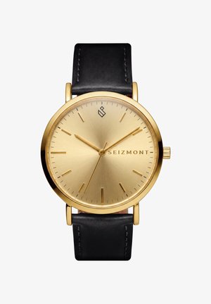 Guld Seizmont armbåndsur med sort læderrem, minimalistisk urskive, gyldne timeindikatorer og tre gyldne visere, der viser 10:10:37.