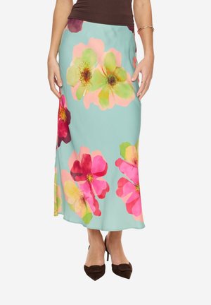 Mujer con una falda midi azul claro con grandes estampados florales en rosa, rojo y amarillo, combinada con tacones negros de punta afilada.