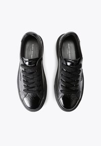 Une paire de sneakers en cuir noir à lacets de Kurt Geiger avec une finition texturée et brillante, présentée de dessus sur un fond blanc.