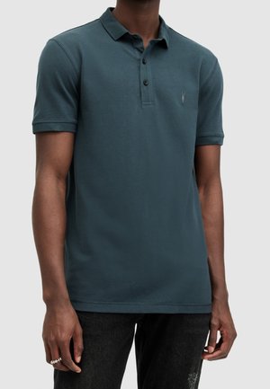 Mørk teal poloshirt lavet af bomuldsblanding, med en tre-knaps lukning, korte ærmer og en lille logo på brystet.
