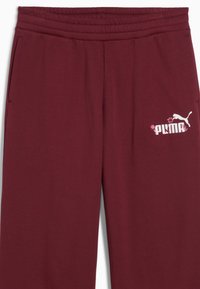 Burgundowe spodnie dresowe wykonane z miękkiego materiału, z elastycznym paskiem w talii, bocznymi kieszeniami oraz białym logo Puma z kwiatowymi akcentami.