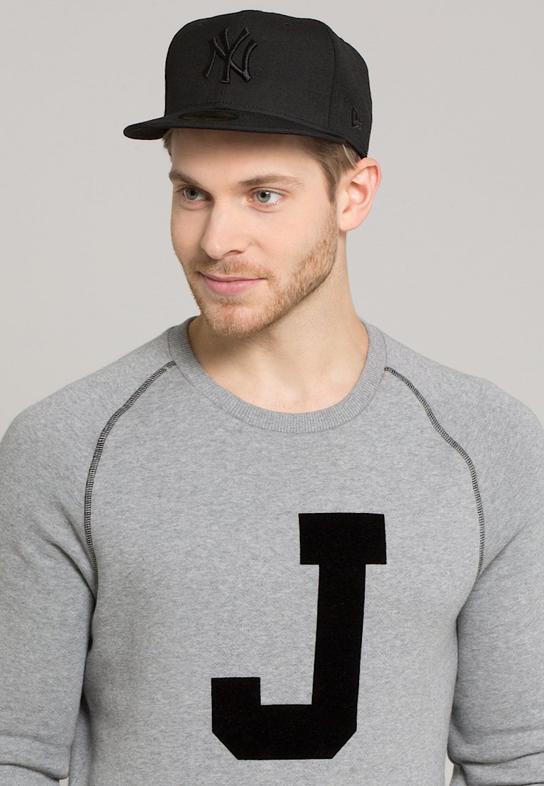 Sudadera gris con emblema negro de "J" en el frente y costuras en contraste. Gorra de béisbol negra con el logo de Nueva York en relieve.