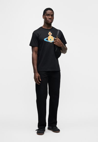 Μαύρο βαμβακερό t-shirt με γραφικό ενός αστροναύτη και πλανήτη σε κίτρινο και μπλε χρώμα, συνδυασμένο με μαύρο παντελόνι και σκούρα παπούτσια.