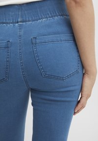 Jeans de mezclilla azul con una banda elástica de talle alto, con dos bolsillos traseros y una textura suave. Vista trasera que muestra el ajuste y los detalles de la costura.