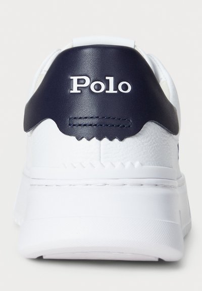 Hvite sneakers med en marineblå skinnakcent ved hælen. Har "Polo"-logoen i hvitt, teksturert mønster på baksiden.