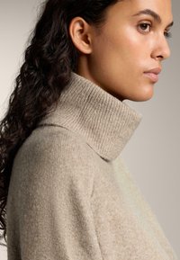 Pulover bej cu guler înalt dintr-un tricot moale, texturat, cu un guler elastic, având o croială lejeră și cusături minime.