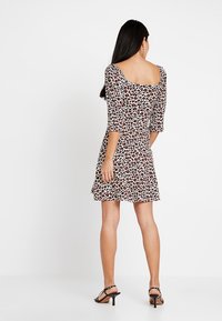 Šaty s leopardím vzorem, tříčtvrtečním rukávem, čtveratým výstřihem na zádech a rozšířenou sukní. Vyrobené z elastického materiálu, s bílým pozadím.