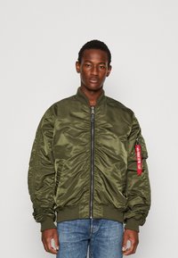 Olive green bomber jacket made from shiny fabric, featuring a zip front, ribbed cuffs, and waistband, with a red tag on the sleeve.