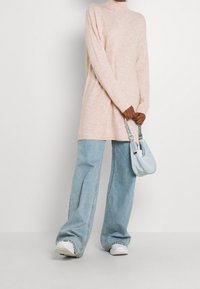 Helles rosa gestricktes Rollkragenkleid, kombiniert mit weit geschnittenen hellblauen Jeans und weißen Sneakers. Kleine hellblaue Tasche mit Schulterriemen.