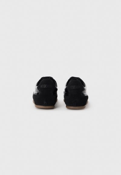 Black patent leather sneakers with suede accents, featuring a curved design, and beige rubber soles. Logo embossed on the heel.