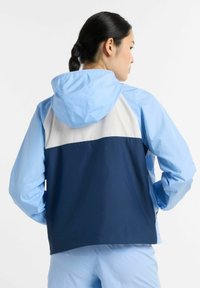 Ljusblå huva jacka med en marinblå nederdel och en vit övre panel. Tillverkad av mjukt, lätt tyg med långa ärmar.