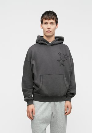Charcoal grey hoodie with a large front pocket, hood, and embossed star details; paired with light grey sweatpants. Cotton blend fabric.
