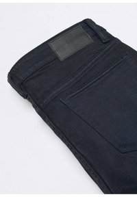Tmavě modré džíny vyrobené z denimu, s zadní kapsou, obdélníkovou koženou nášivkou na pase a viditelnými detaily šití.