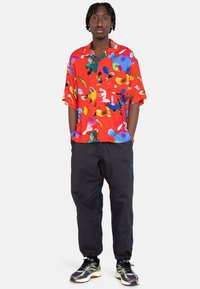 Short-sleeve red shirt with colorful abstract patterns, paired with dark loose-fit pants and multicolored running shoes.