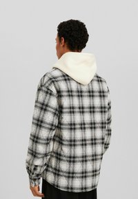 Svartvitt rutig skjorta med en vadderad textur, med en beige huva som kikar fram bakom, knäppta manschetter och avslappnad passform.