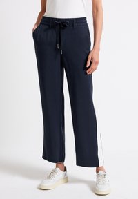 Navy vida-långa byxor med elastisk midja och dragsko, med vita sidostenar. Tillsammans med vita sneakers.