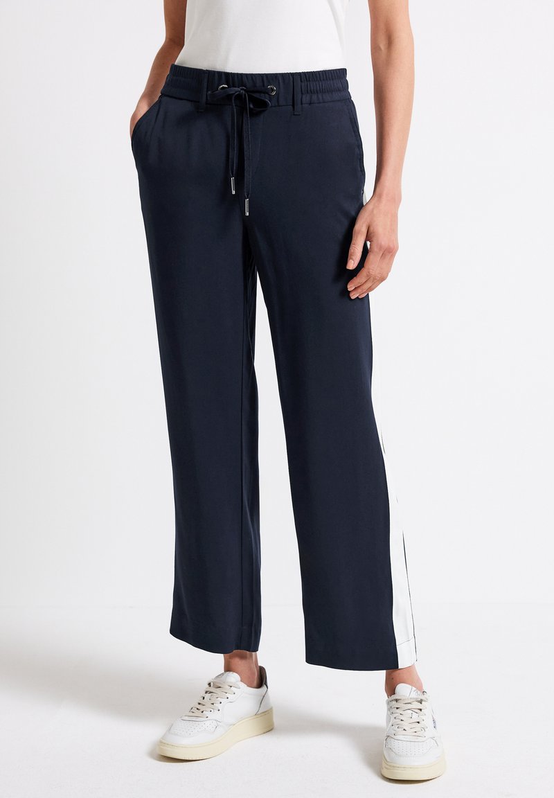 Navy vida-långa byxor med elastisk midja och dragsko, med vita sidostenar. Tillsammans med vita sneakers.