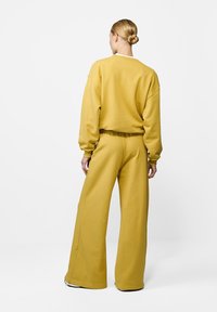 Żółta, oversize'owa bluza z bawełny oraz spodnie szerokie z mieszanki bawełny, z prążkowanymi mankietami i luźnym krojem, pokazane od tyłu.