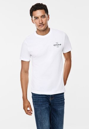 Witte katoenen t-shirt met ronde hals, korte mouwen en zwarte geprinte tekst "VINYL CLUB" op de linkerborst. Gekozen in combinatie met donkerblauwe spijkerbroek.
