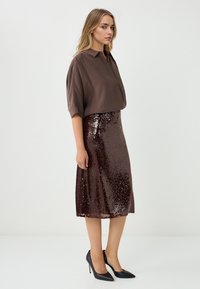 Braune Knopfleiste-Hemd, glitzernder brauner Rock, schwarze High Heels. Glattes Gewebe oben, glänzende Pailletten in verschiedenen Größen auf dem Rock.