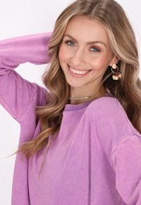 Felpa oversized viola con una vestibilità ampia, scollatura rotonda e texture morbida; presenta orecchini a strati con accenti circolari e floreali.