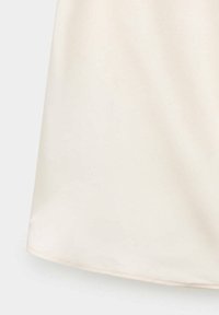 Gros plan de la partie inférieure d’un tissu couleur crème avec une texture lisse et un ourlet cousu au bord inférieur.